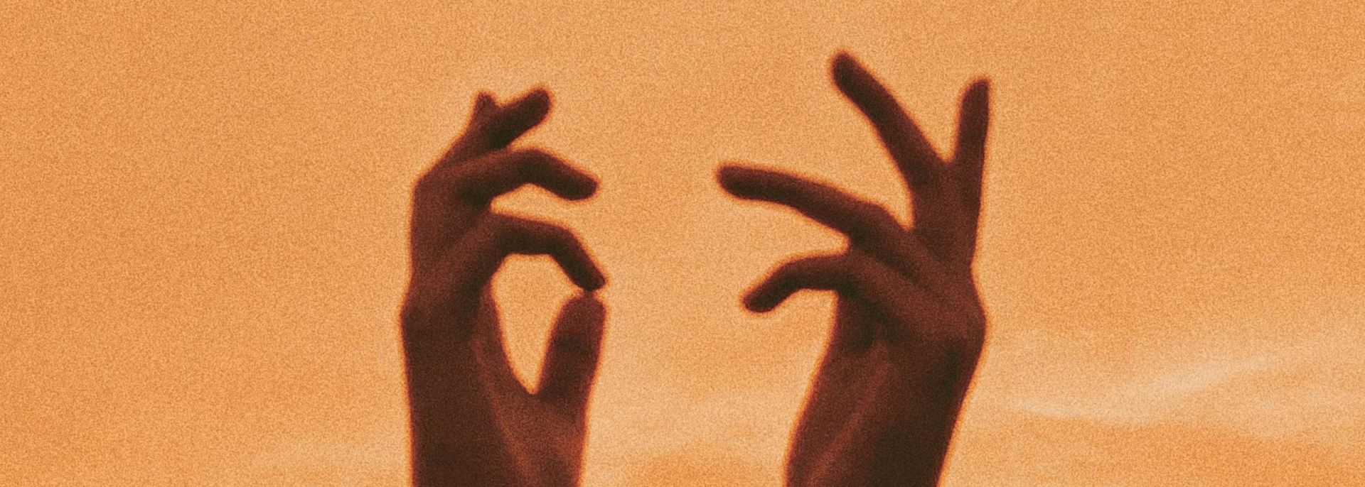 Silhouetted hands reaching up towards the moon and a shooting star in a warm orange sky.