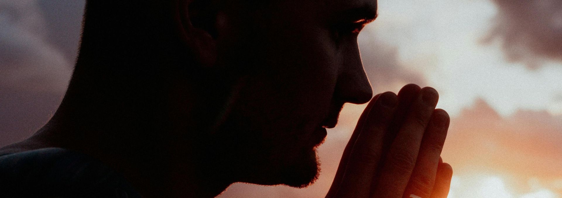 A serene silhouette of a man praying by the beach during a beautiful sunset.